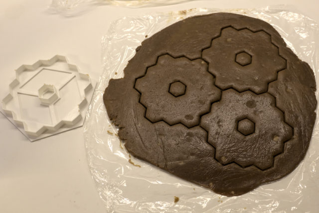 Flat, uncooked gingerbread dough with three cookies cut out and cookie cutter next to the dough
