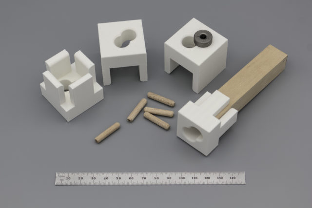 White 3D-printed parts that hold a drill bushing and can be clamped to a square wood dowel