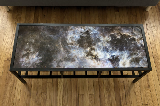 Black wooden coffee table with image of Tarantula Nebula on top and slats on the bottom, viewed from top