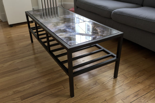 Black wooden coffee table with image of Tarantula Nebula on top and slats on the bottom, viewed from end