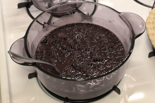 Pot on stove top containing a blackberry mixture and a fork for stirring