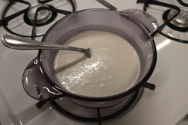 Pot on stove top containing a coconut milk mixture and a fork for stirring