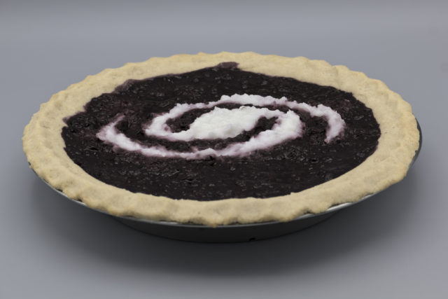 Side view of pie with a light crust, dark filling, and a white spiral galaxy inset in the filling