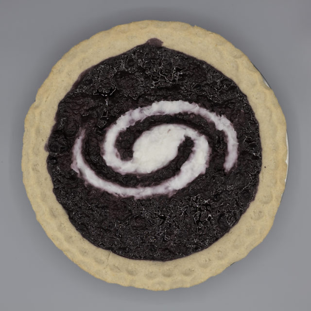 Top view of pie with a light crust, dark filling, and a white spiral galaxy inset in the filling