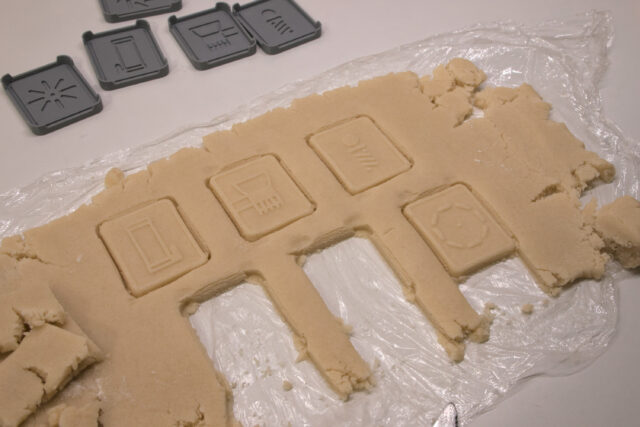Four cookie designs are shown pressed into rolled out dough, and empty rectangles exist where two other cookies have been cut out and removed