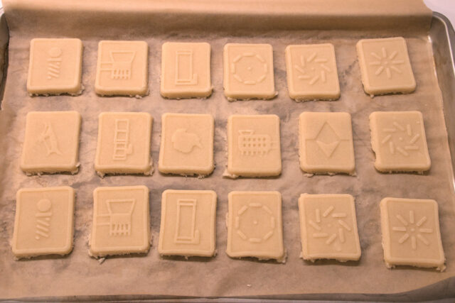 Twelve raw cookies with raised designs are arranged on a parchment-paper-lined baking sheet