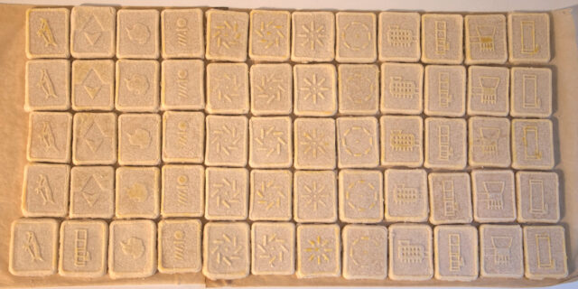 60 cookies with raised designs are arranged in a tight grid on parchment paper