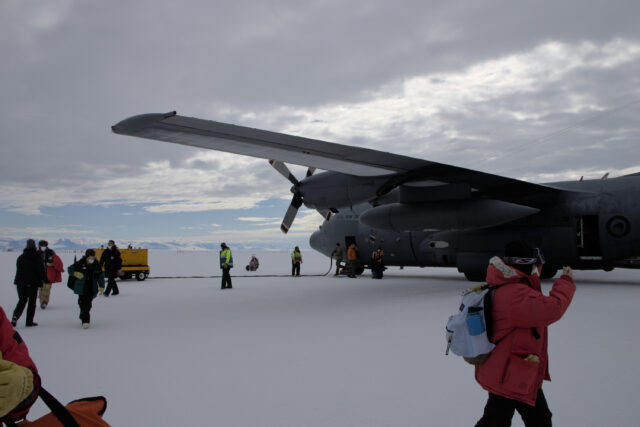 People disembarking from a C-130 parked on an ice sheet.