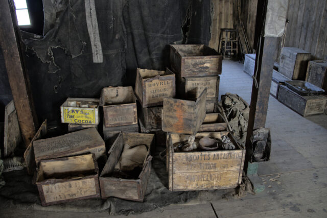 Old wooden boxes with supplies piled on a wooden floor. One reads "Scott's Antarctic Expedition 1910," and another reads "Bovril Sledging Rations."
