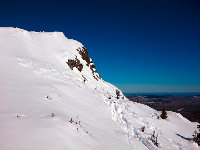 Footprints are seen in snow below a rocky, snow-covered ridgeline