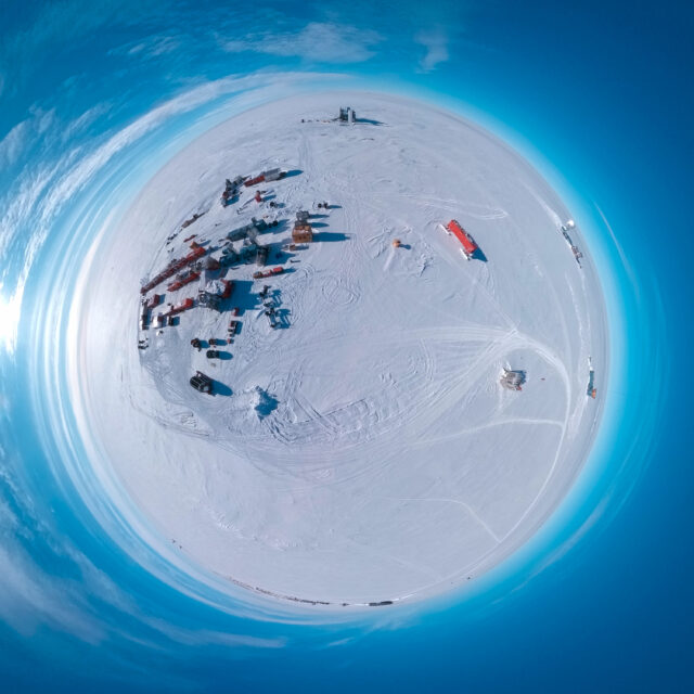 Aerial "little planet" view of a set of shipping-container-sized buildings on an ice sheet.